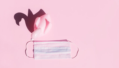 Pink flamingo and medical mask on pink background. Concept of summer holidays and travel in the conditions of the pandemic covid-19.
