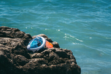 Fototapeta na wymiar A full-face mask for snorkeling lies on a stone. Sea shore, waves of blue water, ocean. The concept of rest and vacation. Place for text, space for vstaki. Blue color.