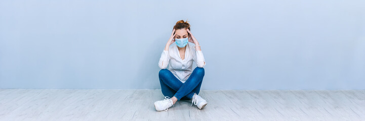 Banner Girl with a medical mask sitting on the floor against the background of a gray wall. The concept on the theme of coronavirus COVID-19.