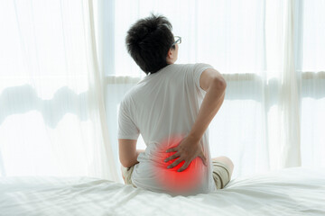 An Asian man is sitting on a couch with back pain.