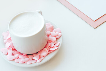 Cappuccino cup decorated with pink hearts and tablet folder on white background
