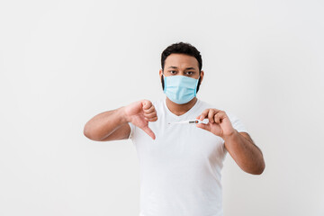 sick african american man in medical mask holding digital thermometer and showing thumb down near white wall