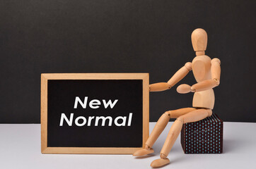 Wooden figure with text "NEW NORMAL" on black background.