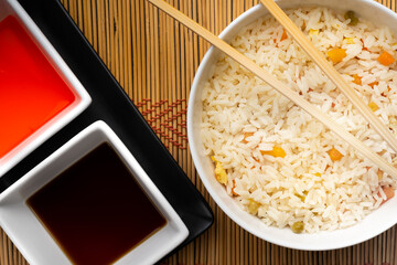 Chinese food bowl of rice with chopsticks and soy sauce and sweet and sour sauce on bamboo trivet and black background