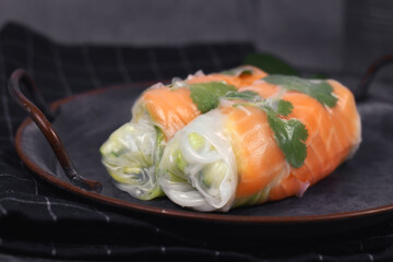 Two pieces of traditional Vietnamese spring rolls fied with salmon, avocado,  salad and rice noodles on dark dish