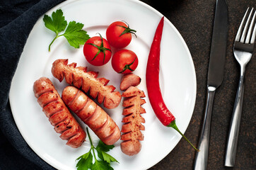 
classic grilled sausages on a white plate with
 tomatoes with spices and herbs on a stone background