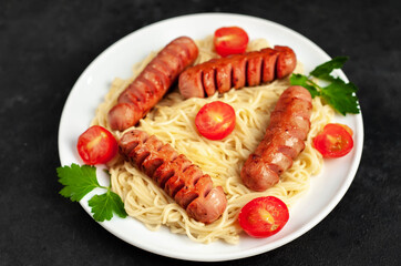 
Italian
pasta with classic grilled sausages on a white plate with
 tomatoes with spices and herbs on a stone background