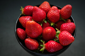 Fresh ripe strawberries in a black bowl isolated on neutral background, top view.