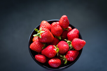 Fresh ripe strawberries in a black bowl isolated on neutral background, top view.