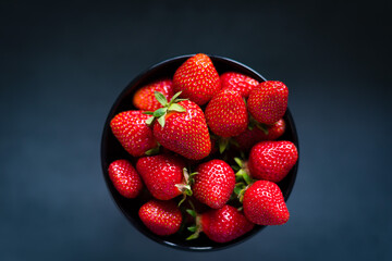 Fresh ripe strawberries in a black bowl isolated on neutral background, top view.