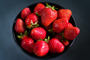 Fresh ripe strawberries in a black bowl isolated on neutral background, top view.