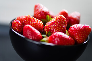 Fresh ripe strawberries in a black bowl isolated on neutral background, top view.