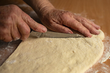 Obraz premium Grandmother's hands cut with a knife raw homemade dough for baking. Side view.