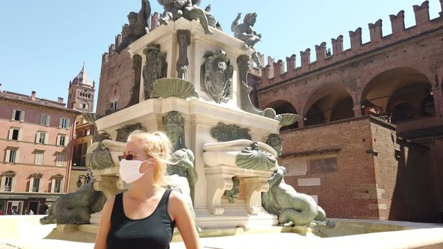 Lifestyle woman with the surgical mask in Maggiore square with Neptune statue and San Petronio basilica. Coronavirus after COVID-19 lockdown with social distancing in Bologna city of Italy.