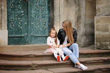 A mother and her little daughter are sitting on the steps of an old church.