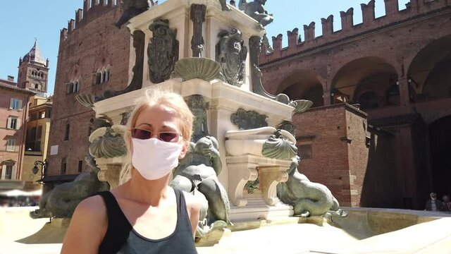 Lifestyle tourist girl with the surgical mask in Maggiore square at Neptune statue and San Petronio basilica. Coronavirus after COVID-19 lockdown with social distancing in Bologna city of Italy.