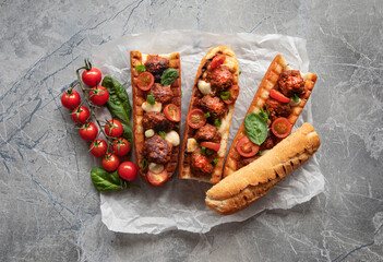 Delicious sandwich with meatballs on a baguette, with melted cheese, tomato sauce, parsley and Parmesan cheese on top. Italian meatballs baked in a baguette on a marble table. The view from the top. 