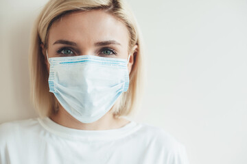 Close up photo of a caucasian woman with medical mask and blonde hair looking at camera near white free space