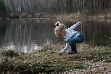 Naklejka na ściany i meble Little girl in rubber boots catches and feeds fish on the river in a jar