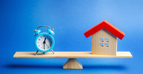 A clock and a miniature house on the scales. Mortgage and loan concept. Real estate and risks....