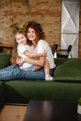 cute daughter hugging cheerful and curly mother