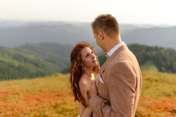 The bride and groom hug and tenderly with each other. Sunset. Wedding photo on a background of autumn mountains. A strong wind inflates hair and dress. Close-up.