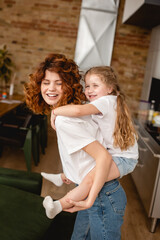 positive and curly mother piggybacking cute daughter