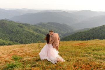 The groom kisses the bride on the lip. Sunset. Wedding photo on a background of autumn mountains. A strong wind inflates hair and dress.