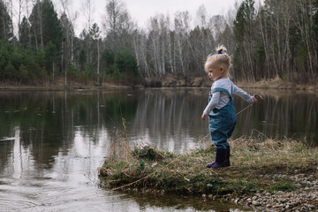 Naklejka na ściany i meble Little girl in rubber boots catches and feeds fish on the river in a jar
