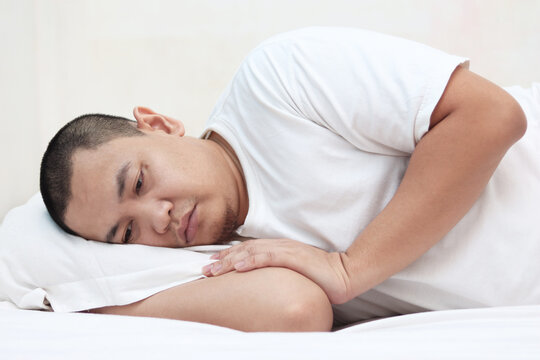 Sad unhappy Asian man lying on bed with blank stare, hard to sleep thinking of bad situation
