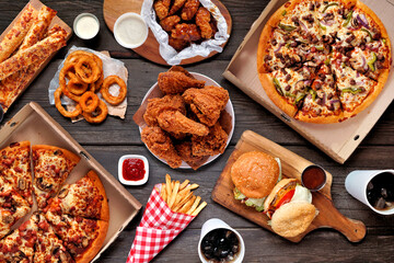 Buffet table scene of take out or delivery foods. Pizza, hamburgers, fried chicken and sides. Above...