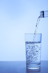 fresh clean water is poured from a bottle into a glass cup. Light background.