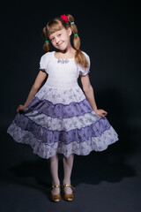 A little girl in a dress with ponytails poses against a dark background