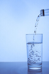fresh clean water is poured from a bottle into a glass cup. Light background.