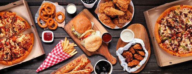 Table scene of assorted take out or delivery foods. Hamburgers, pizza, fried chicken and sides. Top...