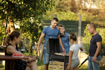 People, food ang leisure concept. Family with friends cooking meat on barbecue grill in the garden  at summer