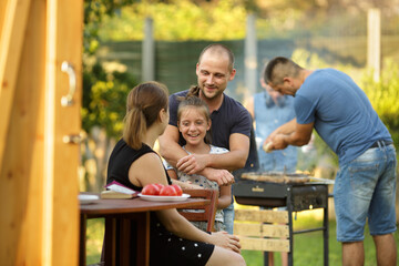 People, food ang leisure concept. Family with friends cooking meat on barbecue grill in the garden  at summer
