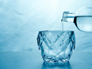 fresh clean water is poured from a bottle into a glass cup. Light background.