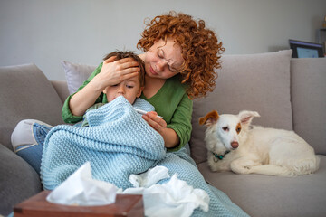 Mother taking care of sleepy child while sitting on couch in the living room. The mother is...