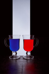 silhouettes of two glasses on a black and white background. Blue and red liquid