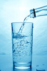 fresh clean water is poured from a bottle into a glass cup. Light background.