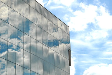 the corner part of the building is made entirely of glass and metal. The glass beautifully reflects the clouds in the blue sky