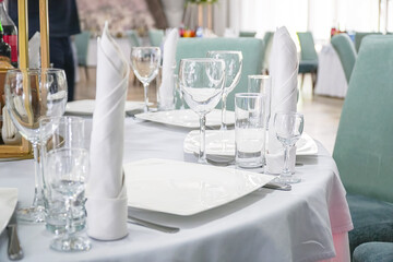 The table in the restaurant is served for dinner. On a table with a white tablecloth, empty wine glasses, a plates, napkins. Selective focus