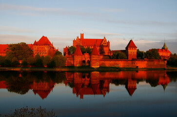 Naklejka na ściany i meble Mighty castle of the Teutonic Knights Order in Malbork (Poland, historical Prussia) on a dawn. The biggest brick gothic fortress in the world, UNESCO world heritage site. Fairy-tale medieval castle. 