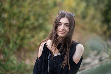 Beautiful woman with brunette hair in dark clothes and sunglasses. Fashion street photography. Fashion model is posing on nature background.