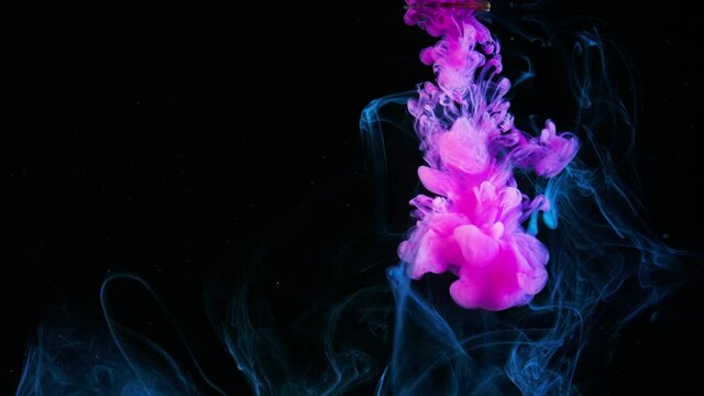 Gentle flow of paint in water. Stock footage. Close-up of beautiful pink ink floating smokily in water on black background. Slow motion paint in water