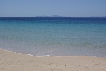 A quiet Mediterranean beach on the Greek island of Donoussa on a summers day.  The horizon in the...