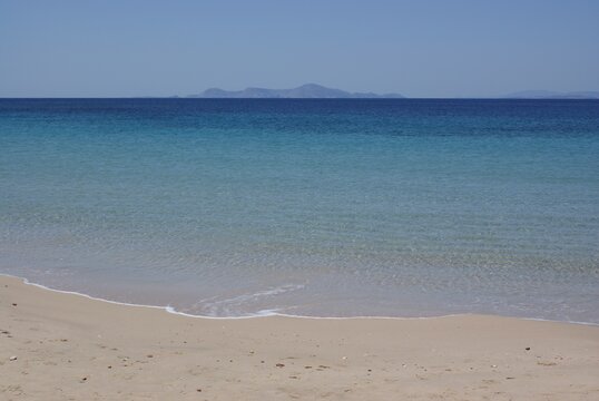 A quiet Mediterranean beach on the Greek island of Donoussa on a summers day.  The horizon in the distance with crystal clear blue sea waters lapping onto a pristine beach.  Copy space.