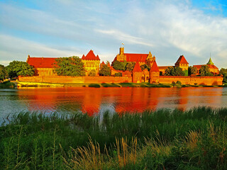 Naklejka na ściany i meble Mighty castle of the Teutonic Knights Order in Malbork (Poland, historical Prussia) on a dawn. The biggest brick gothic fortress in the world, UNESCO world heritage site. Fairy-tale medieval castle. 