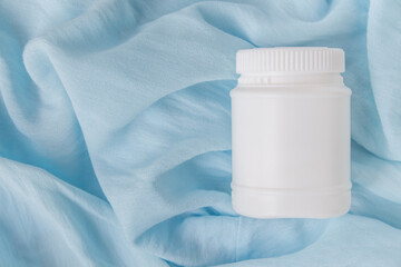 Creative layout on a blue background. White cosmetic jar with shadow. Stylish look of the product. Card with copy space